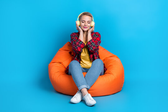 Full size photo of nice girl with short hairstyle wear red shirt sit in armchair arms touch headphones isolated on blue color background