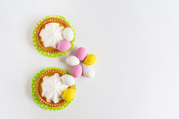 Obraz na płótnie Canvas Two Easter tartlets decorated with sweets Easter eggs on a light background, close-up. Copy space. Easter delicious dessert.