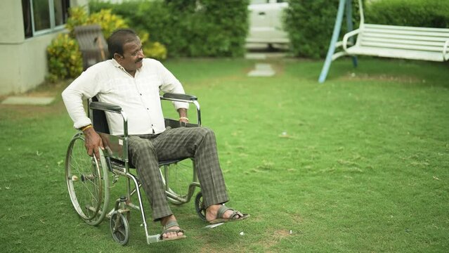 Indian Hindu lonely  senior elder old widower man sitting on wheel chair suffer chronic health issue retired older male enjoy outdoor house garden home park grass health care illness concept