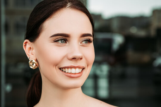Pretty brunette caucasian woman standing outside street with white teeth beaming healthy smiling lady. Happy millennial girl model posing looking at the camera, head shot portrait.
