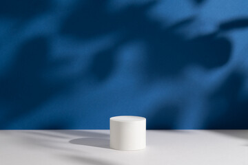 Empty white round podium and deep shadows on dark blue background. Showcase for product presentation. Pedestal for beauty cosmetic advertising. Minimal still life. Front view.