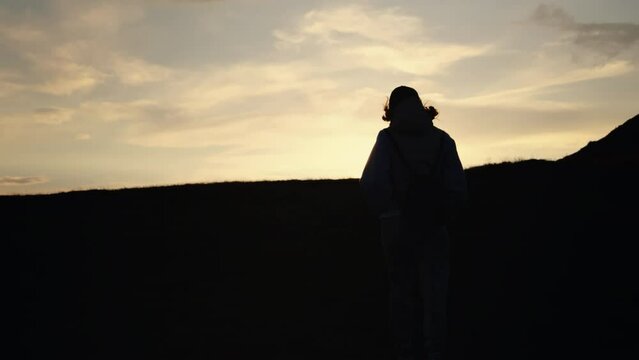 Silhuette Young Woman walking on the mountain observing sunset. Travaler reaching the peak of the mountain at dark.