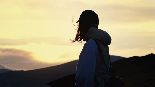 Back view of woman with cap and packpack admiring twilight. Silhuette Woman on top of the mountain.