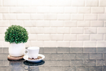 Espresso cup and saucer with dark roasted coffee beans with modern counter and white subway tile reflection in cafe bar kitchen with green plant