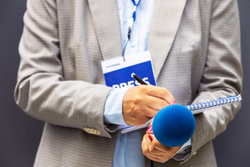Journalist correspondent or reporter with press pass at media event, holding microphone, writing...