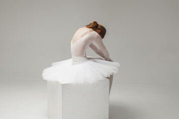 attractive woman, ballerina in white ballet dress sitting on cube, studio shot © Sergey Chumakov