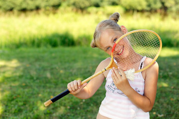 European blonde girl with badminton racket smiles cheerfully. Summer vacation concept. Children in the summer.