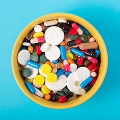 Pile of pills in a bowl on a blue background, top view. The concept of filling natural products with medicines