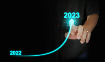 A man's finger draws an upwards curved line from 2022 to 2023. New Year, Christmas, start-up, new business, setting a personal goal