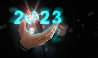 Businessman's hand holding the year 2023 with light blub, dart, and target. Starting new year, business, project, path, goal, or life. Control, manage, choose, and decide by and for yourself.