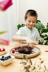 A boy decorates a heart-shaped chocolate cake for mother's day with fresh berries. Valentine's Day