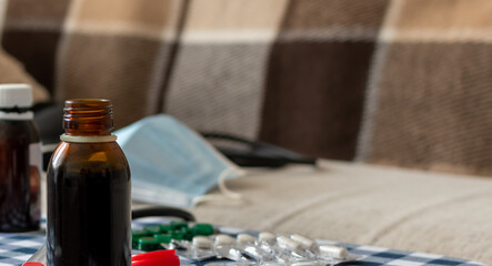 Potions and pills on blurred background of disposable medical mask on sofa at home