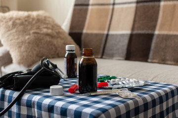 Phonendoscope, thermometer, potions and pills on blurred background of sofa at home