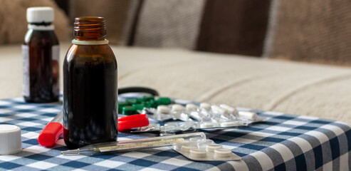 Potions, thermometer and pills on blurred background of sofa at home