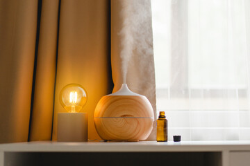 Aromatherapy concept. Aroma oil diffuser on the table against the window. Air freshener. Ultrasonic aroma diffuser for home - obrazy, fototapety, plakaty