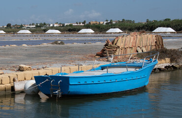 Fototapeta na wymiar Blue boat along a canal of the salt pans of the Stagnone Reserve in Marsala