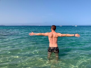 Man with open arms as a sign of freedom. Oceanfront, immersed in the turquoise waters of the Lanzarote sea.