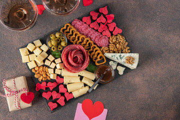 Charcuterie board for Valentines Day with varieties sausage, cheese, nuts, olives and two glass rose wine on brown background - Powered by Adobe