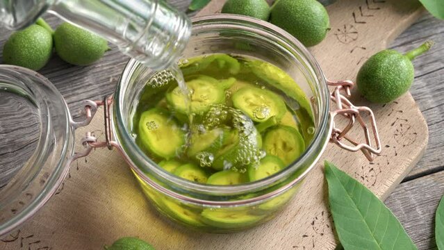 Pouring alcohol into a flass jar filled with green unripe walnuts - preparation of homemade nut liqueur