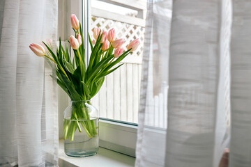 Bouquet of beautiful spring pink tulips in a vase on a windowsill on a sunny day