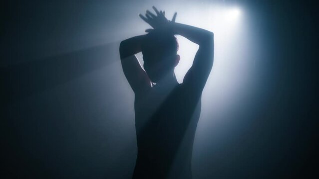 Silhouette of woman with shot hairstyle performing gorgeous dance moves by hands. Graceful fit female dancing in studio with smoke and spotlight. 4K slow motion art concept footage shot on RED camera