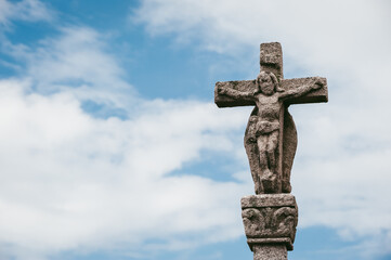 Ancient white stone crucifix with Jesus in cloudy blue sky