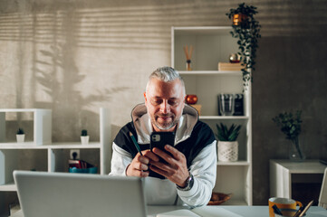 Middle aged man using smartphone and a laptop while working in a home office