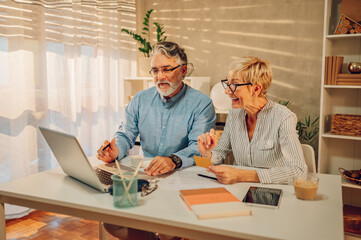 Senior couple online shopping with a credit card and a laptop at home