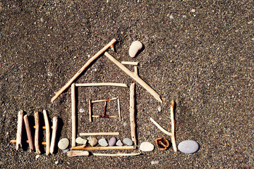 Image of a little house from wooden sticks on the sea pebble beach. Concept image house. Concept of sale or purchase house