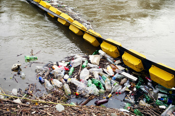 Accumulation of plastic bottles, polystyrene and other waste near the floating barrier in the river