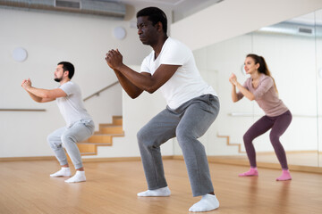 Fototapeta na wymiar Focused adult African American doing warm up before group yoga class in fitness studio