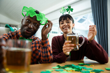 Portrait of happy multiracial friends with beer mugs sitting at table enjoying st patrick's day