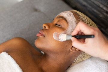 Hand of beautician giving facial to relaxed african american woman with brush