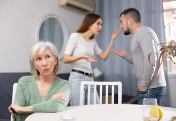 Old woman ignoring her daughter and son-in-law standing behind and arguing with each other at home.