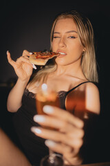 Piękna Kobieta Blondynka jedząca Pizzę z napojem drinkiem w ręce.