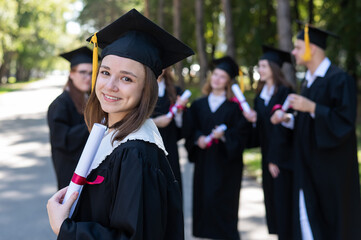Group of happy students in graduation gowns outdoors. A young girl is happy to receive her diploma.