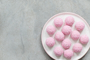 Vegan Strawberry mousse cream candy balls, sprinkled with pink coconut chips. On a plate. Light background. Top view. Copy space
