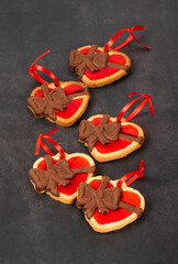 Cute Cookies with a chocolate bow, heart-shaped with strawberry marmalade filling, with a red satin ribbon.  Dark gray background. Valentine's day. 