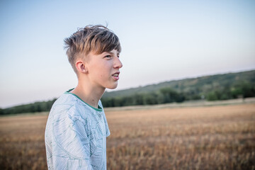 Portrait of a teenager in braces against the background of a field and forest in the summer at sunset.
