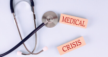 On a blue background, a stethoscope and wooden block with the word MEDICAL CRISIS .Medical concept