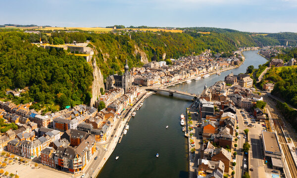 Scenic summer view of Dinant cityscape on banks of river Meuse overlooking Collegiate Church of Notre Dame and fortified Citadel on top of cliff overgrown with green trees, Namur province, Belgium