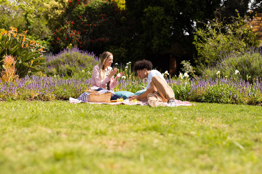 Happy diverse couple relaxing on blanket, having picnic in sunny garden, copy space