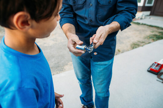 Midsection of father teaching son to tighten nut with spanner at driveway