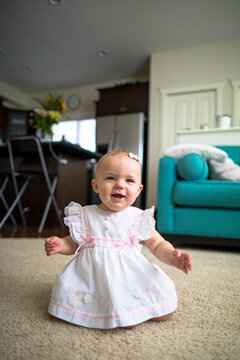 Cute smiling baby girl in dress kneeling on rug at home