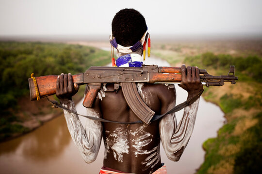 A young man holds his kalashnikov rifle while overlooking the Omo river in the remote Omo Valley of Ethiopia