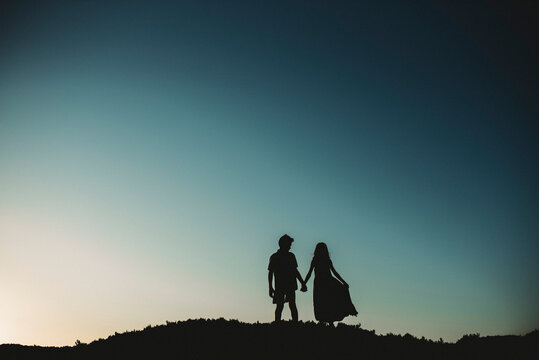 Silhouette of brother and sister standing on sand dune holding hands
