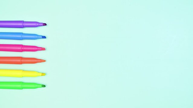 Neon markers pencils appear on left side of pastel turquoise background flat lay stop motion 