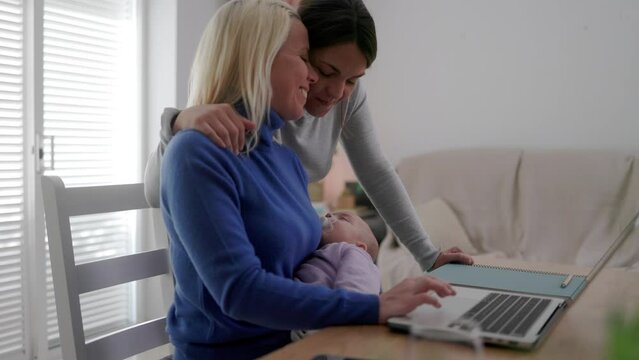 Gay lesbian couple of mothers and newborn baby working with laptop computer at home - Lgbt family concept