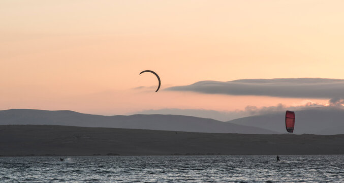 young people kitsurfing in a paracas bay of peru with blue water and drops in the air and mountains in the background-june 2020