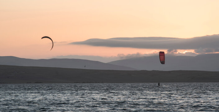 young people kitsurfing in a paracas bay of peru with blue water and drops in the air and mountains in the background-june 2020